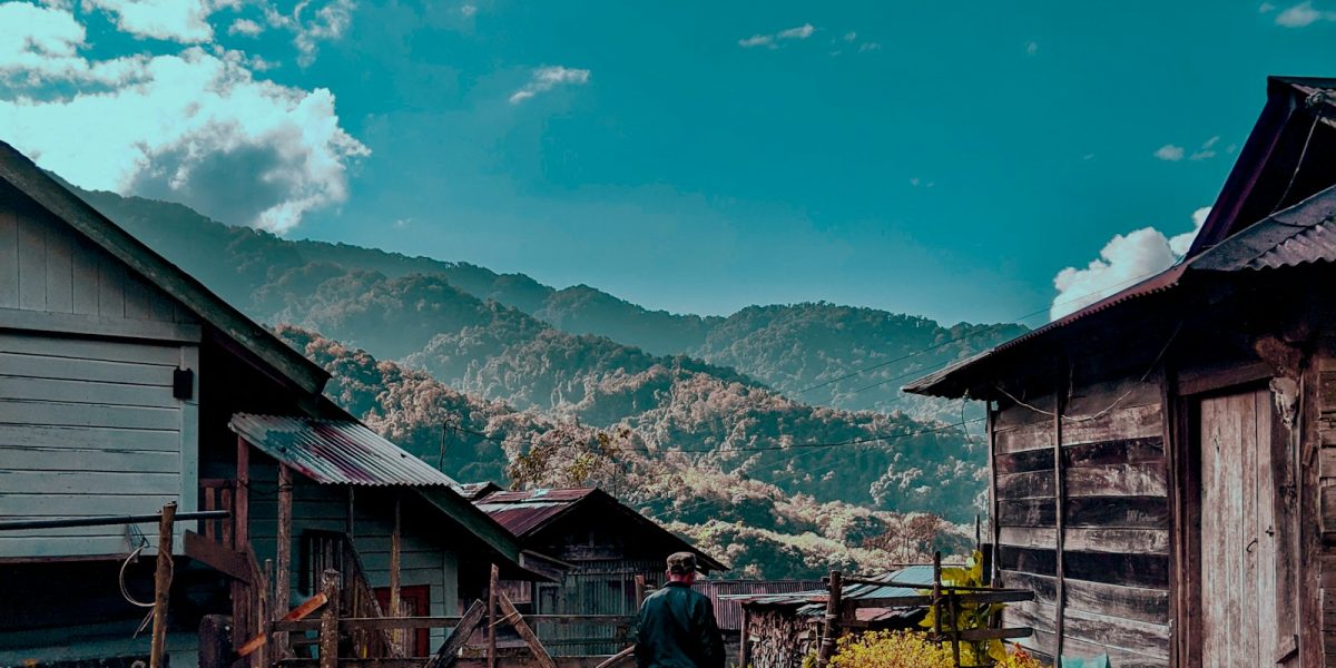 man in black jacket standing near brown wooden house during daytime