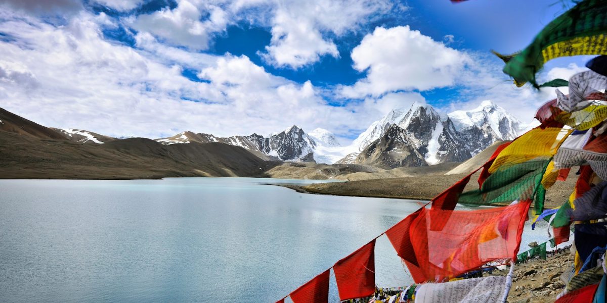 assorted flags on beach shore near snow covered mountains under blue and white sunny cloudy sky